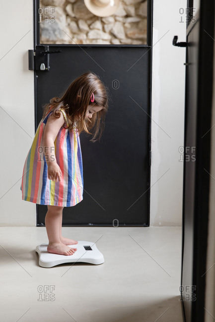 Side view of little girl standing on bathroom scale at home