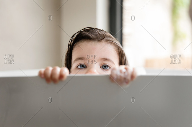 Eyes of toddler girl peeking over bathtub
