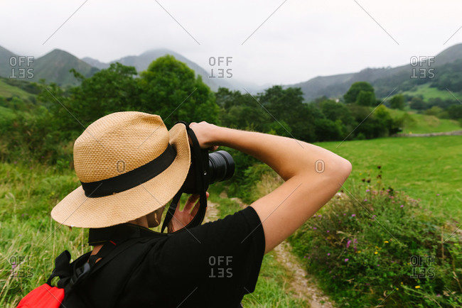 Back view of faceless female tourist taking picture of mountains on photo camera during summer holiday