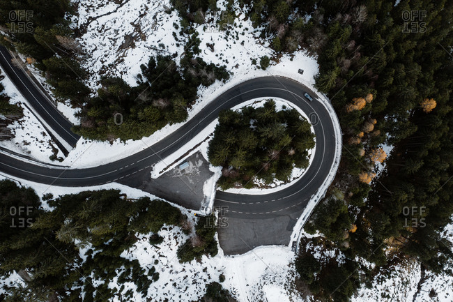 Spectacular drone view of lonely car on road junction in coniferous woods with snow in winter