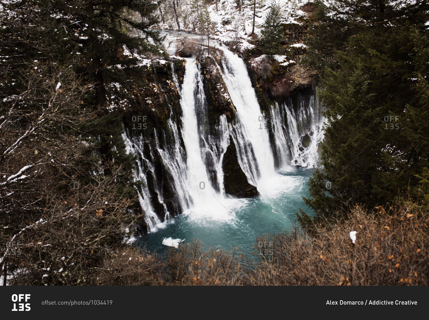 Picturesque scenery of powerful waterfall with pool flowing among snowy forest in mountainous terrain in winter day in USA
