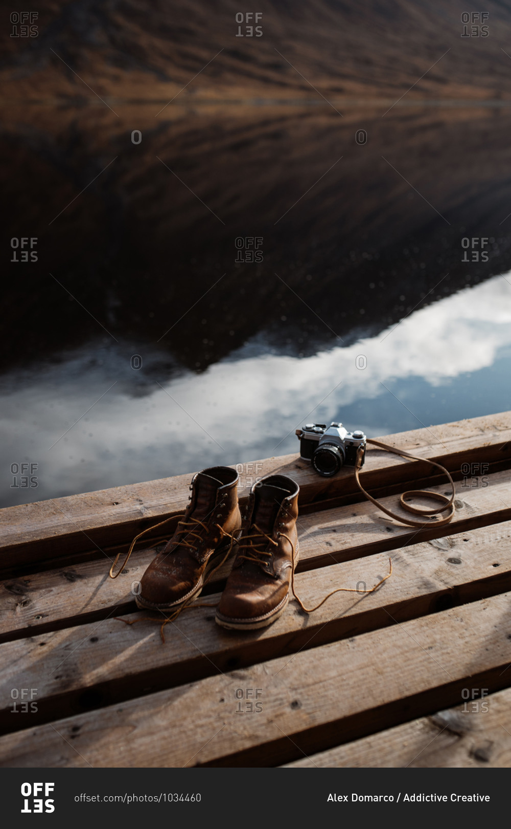 High angle of pair of dirty trekking boots placed on wooden quay near retro photo camera in Scottish Highlands
