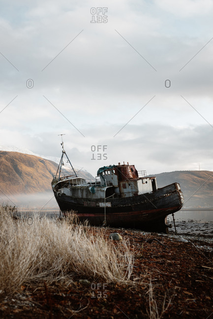 Old rusty fishing boat moored on beach in foggy morning in Scottish Highlands