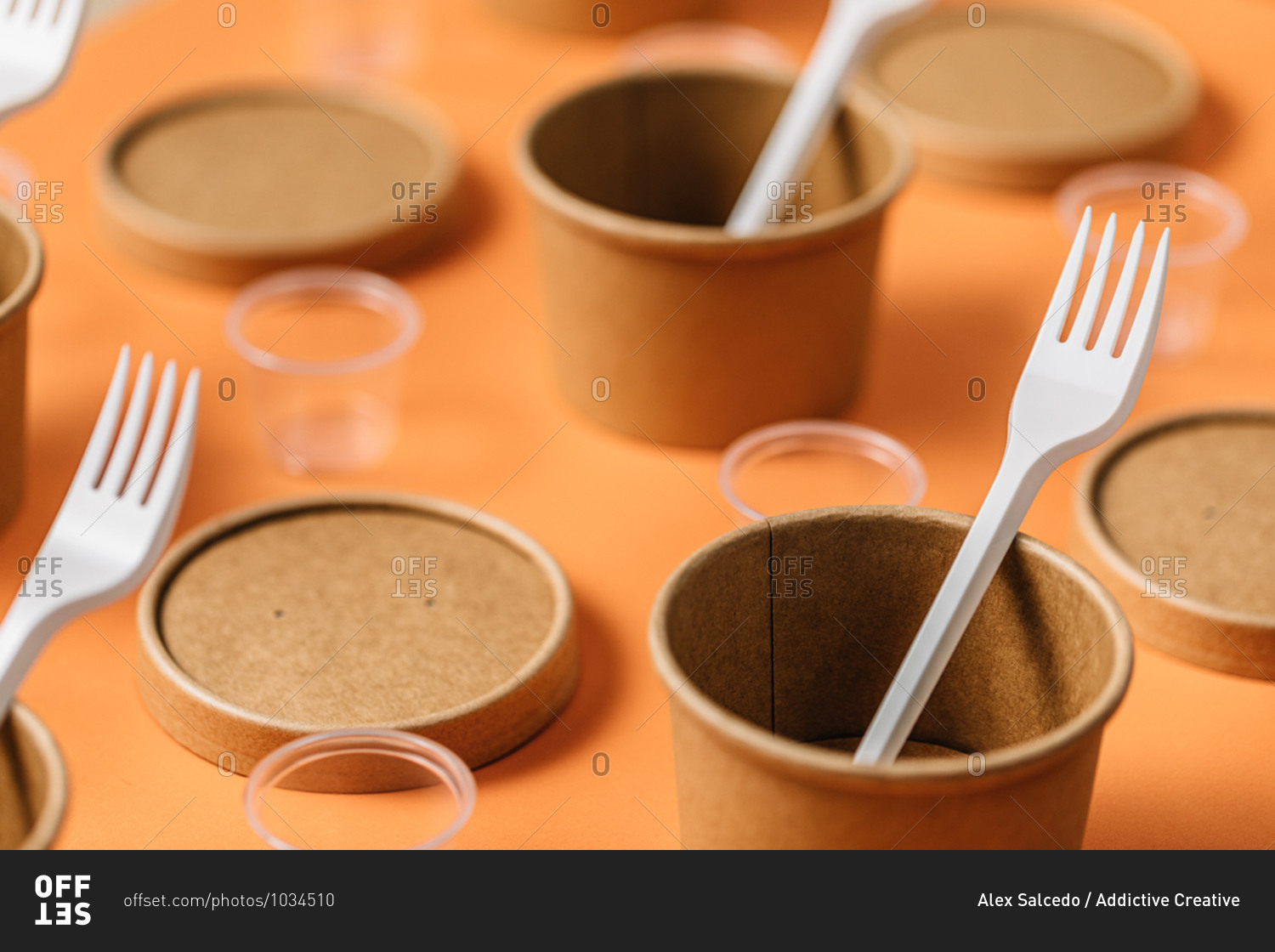 High angle of cardboard containers with plastic forks arranged with small plastic cups for takeaway food service on orange table