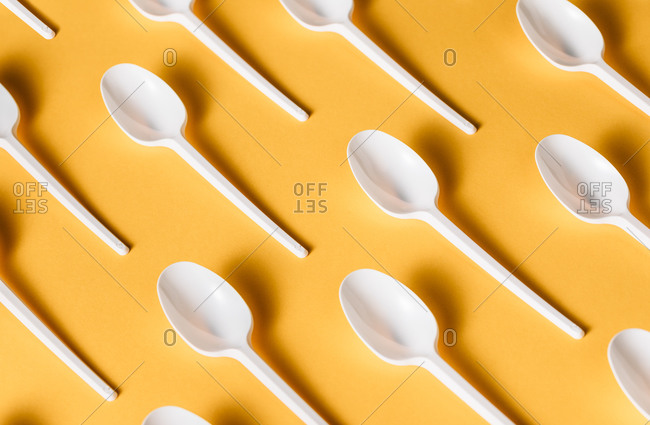 Top view flat lay composition of disposable white plastic spoons for takeaway food arranged on yellow background