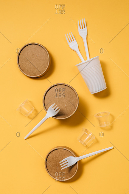High angle of cardboard containers with plastic forks and spoons arranged with small plastic cups for takeaway food service on orange table