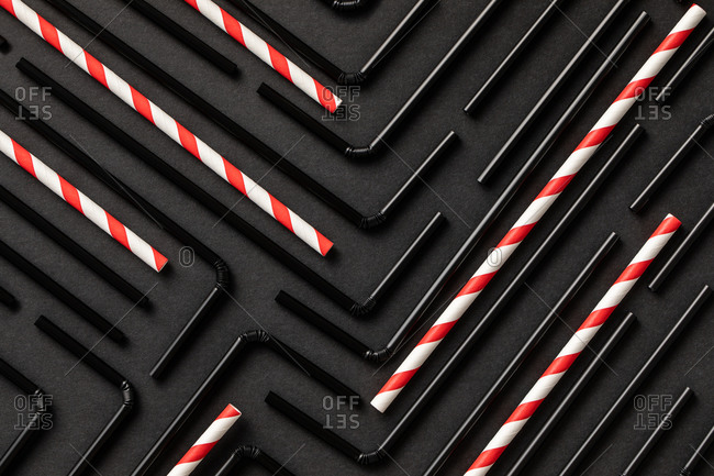 Top view flat lay composition with black and withe and red plastic straws for takeaway drinks arranged in geometric ornament on black background