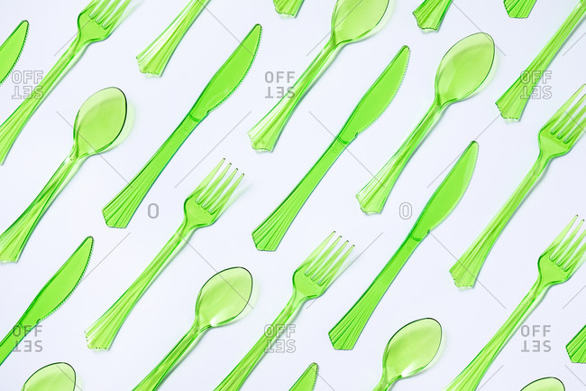 Top view composition of bright green transparent plastic cups with forks and spoons and knives placed on white background