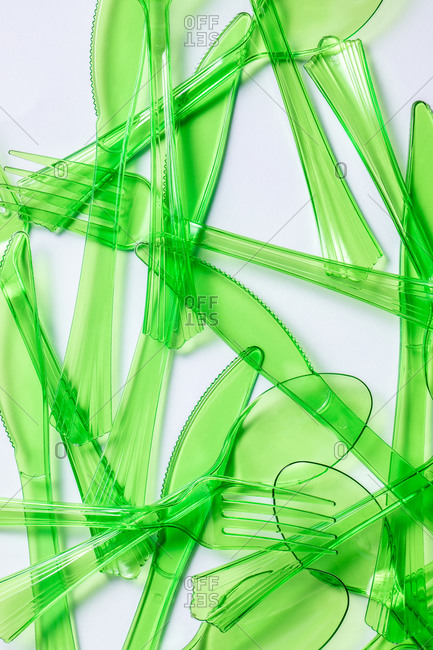 Top view composition of bright green transparent plastic forks and spoons and knives placed on white background