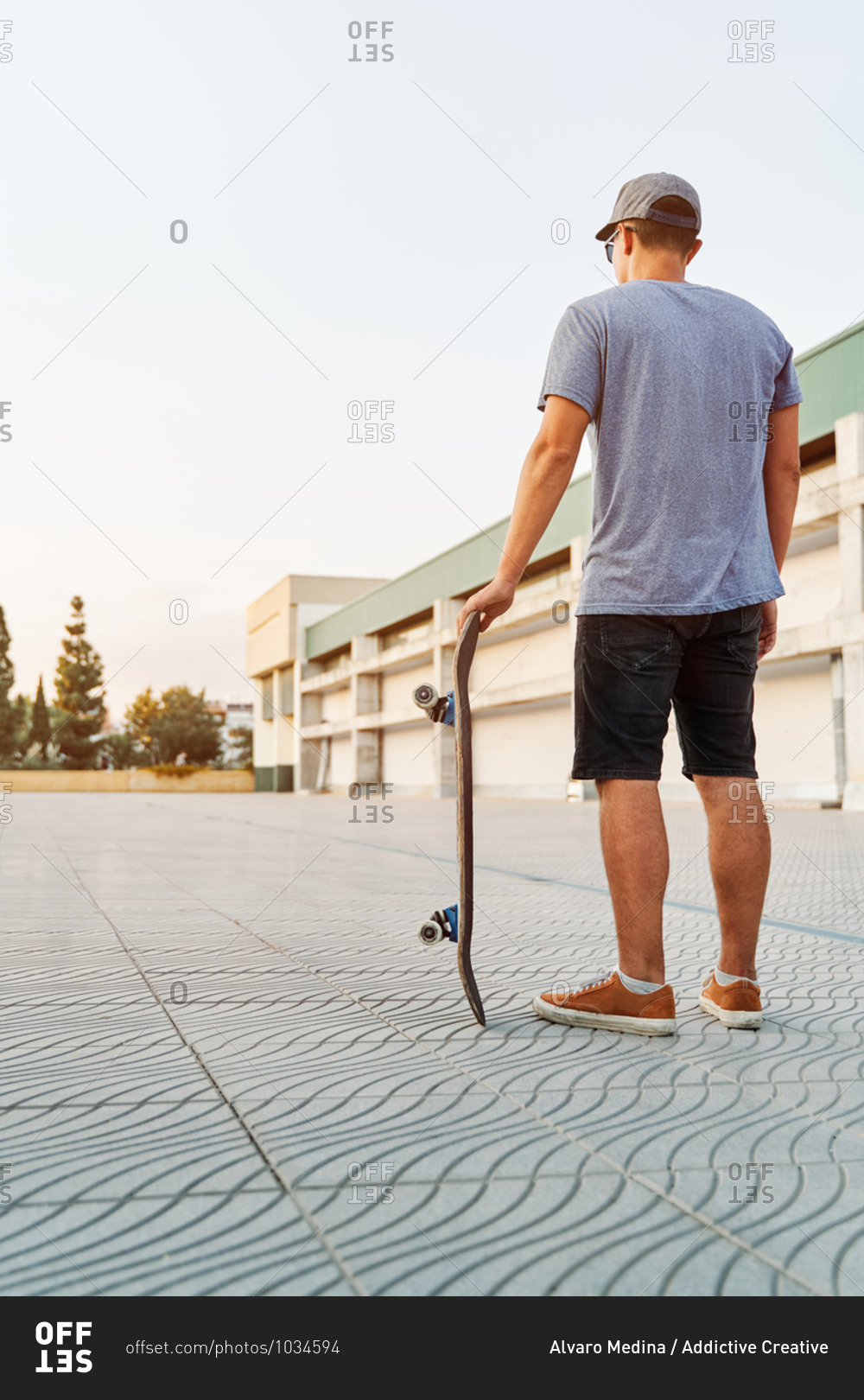 Unrecognizable male in street style outfit standing with skateboard near urban building in city
