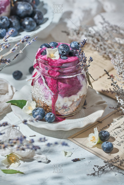 Glass jar with nutritious yogurt with healthy granola and fresh blueberries placed on table for breakfast in morning