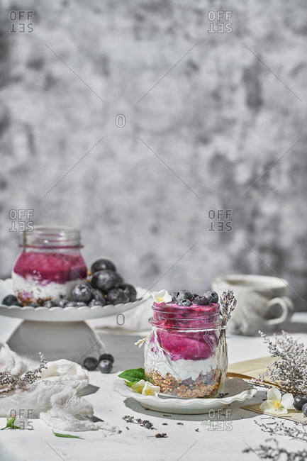 Glass jar with nutritious yogurt with healthy granola and fresh blueberries placed on table for breakfast in morning