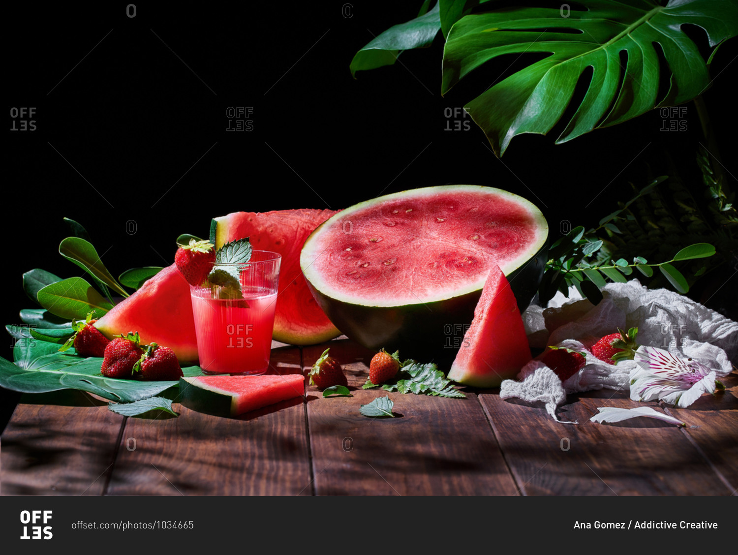 Glass of sweet fruit juice with mint arranged on wooden table with strawberries and ripe watermelon