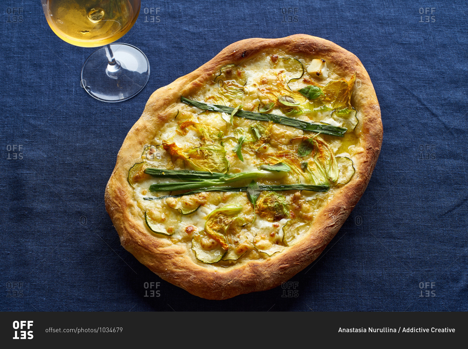 Vegetarian pizza with zucchini flowers, onion, courgette and cheese served with a glass of orange wine