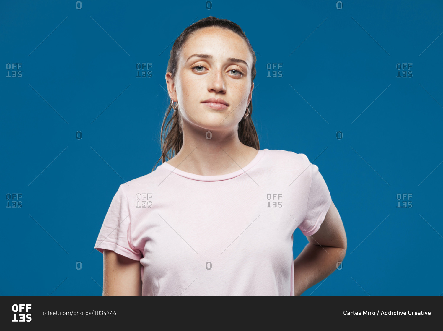 Female teenager model in casual summer clothes standing in blue studio and looking at camera