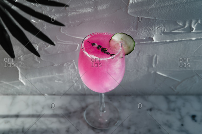 From above of wineglass of refreshing bright purple cocktail garnished with herbs and sliced lime placed in sunlight against blurred gray background