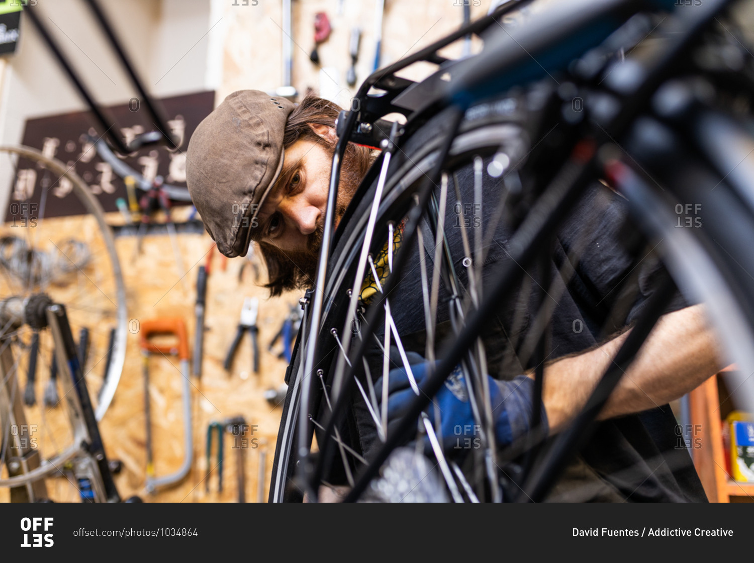 Mature bearded mechanic in workwear and gloves checking and repairing wheel of bike during maintenance service in workshop
