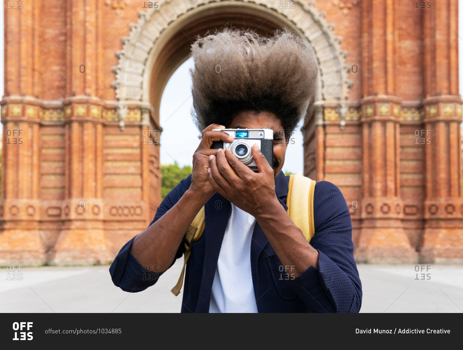 Black man taking a picture while facing the camera with a camera in Arch of Triumph Barcelona