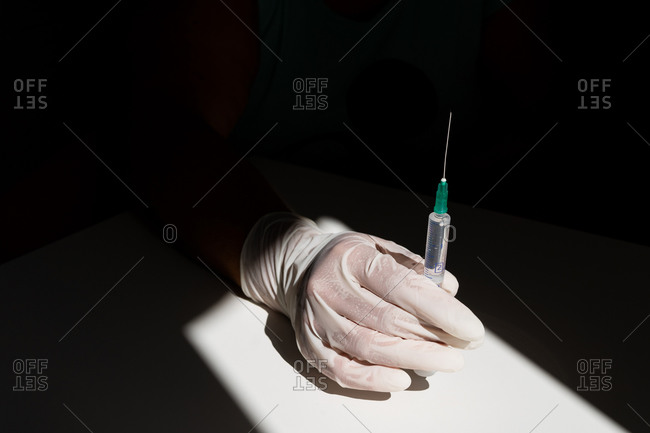 Unrecognizable crop doctor in latex glove demonstrating syringe with drug on black background in studio