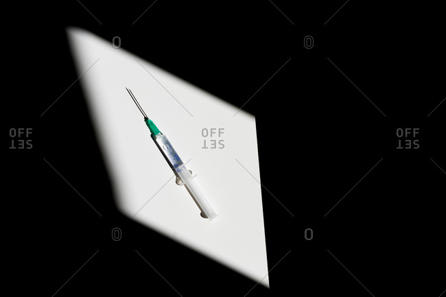 From above sterile syringe with drop of remedy on needle on blurred black background