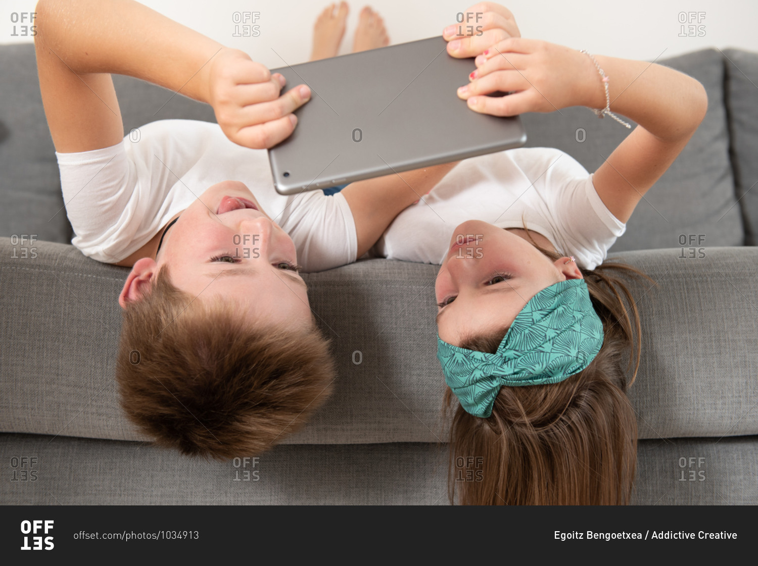 Brother and sister lying face down on the couch while entertained using tablet during weekend
