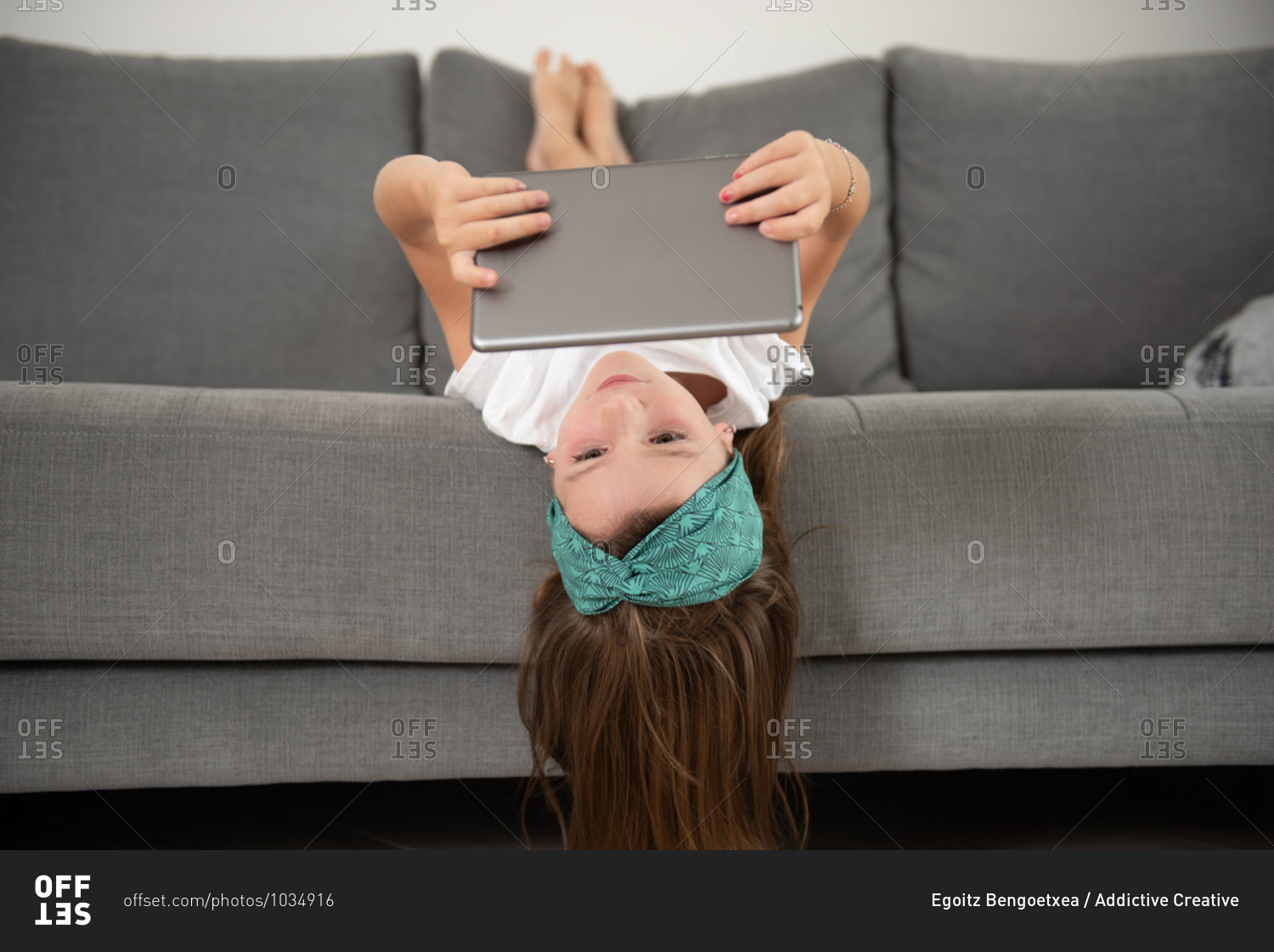 Little girl lying face down on the couch while entertained using tablet during weekend