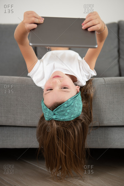 Little girl lying face down on the couch while entertained using tablet during weekend
