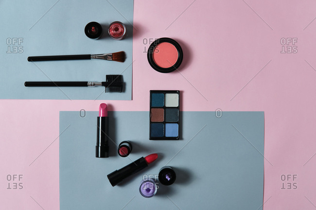 High angle of assorted decorative cosmetics and applicators arranged on two colored background in studio
