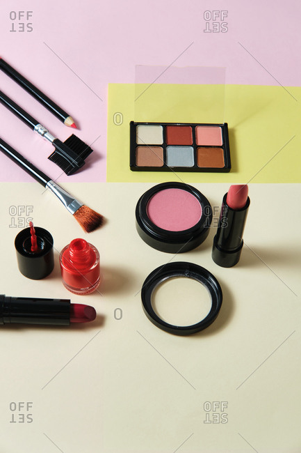 High angle of assorted decorative cosmetics and applicators arranged on three colored background in studio