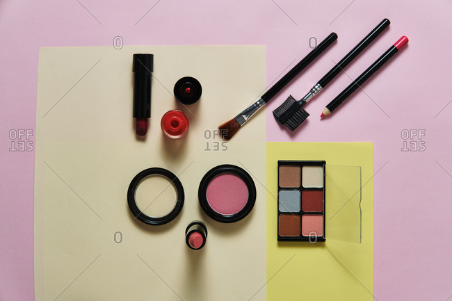 High angle of assorted decorative cosmetics and applicators arranged on three colored background in studio