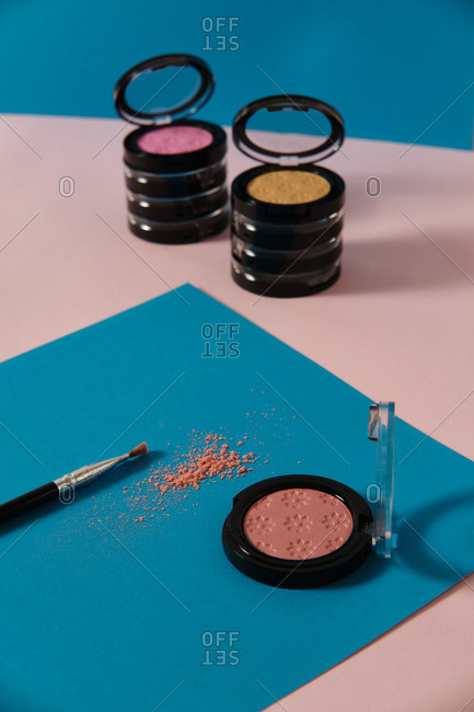 Top view of set of trendy colorful eyeshadows and brush arranged on two colored background in studio