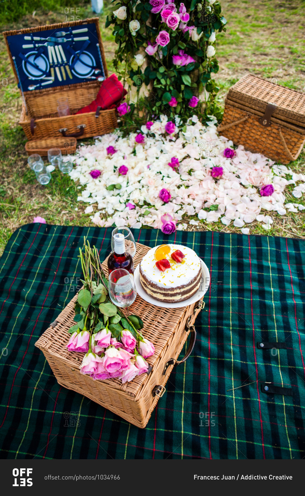High angle of sweet cake and bottle of wine arranged with wineglasses and bouquet of flowers on wicker basket on green lawn for summer picnic