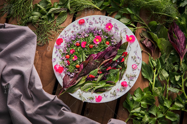 From above of creative composition of delicate flowers and delicious green herbs placed on wooden table with napkin