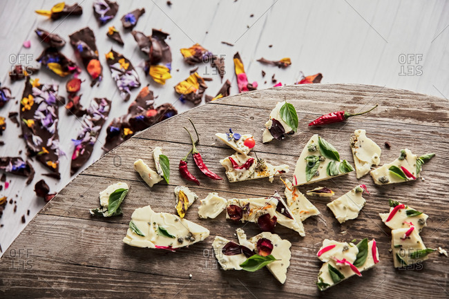 Top view of pieces of tasty chocolate with various flower petals and herbs placed on wooden table