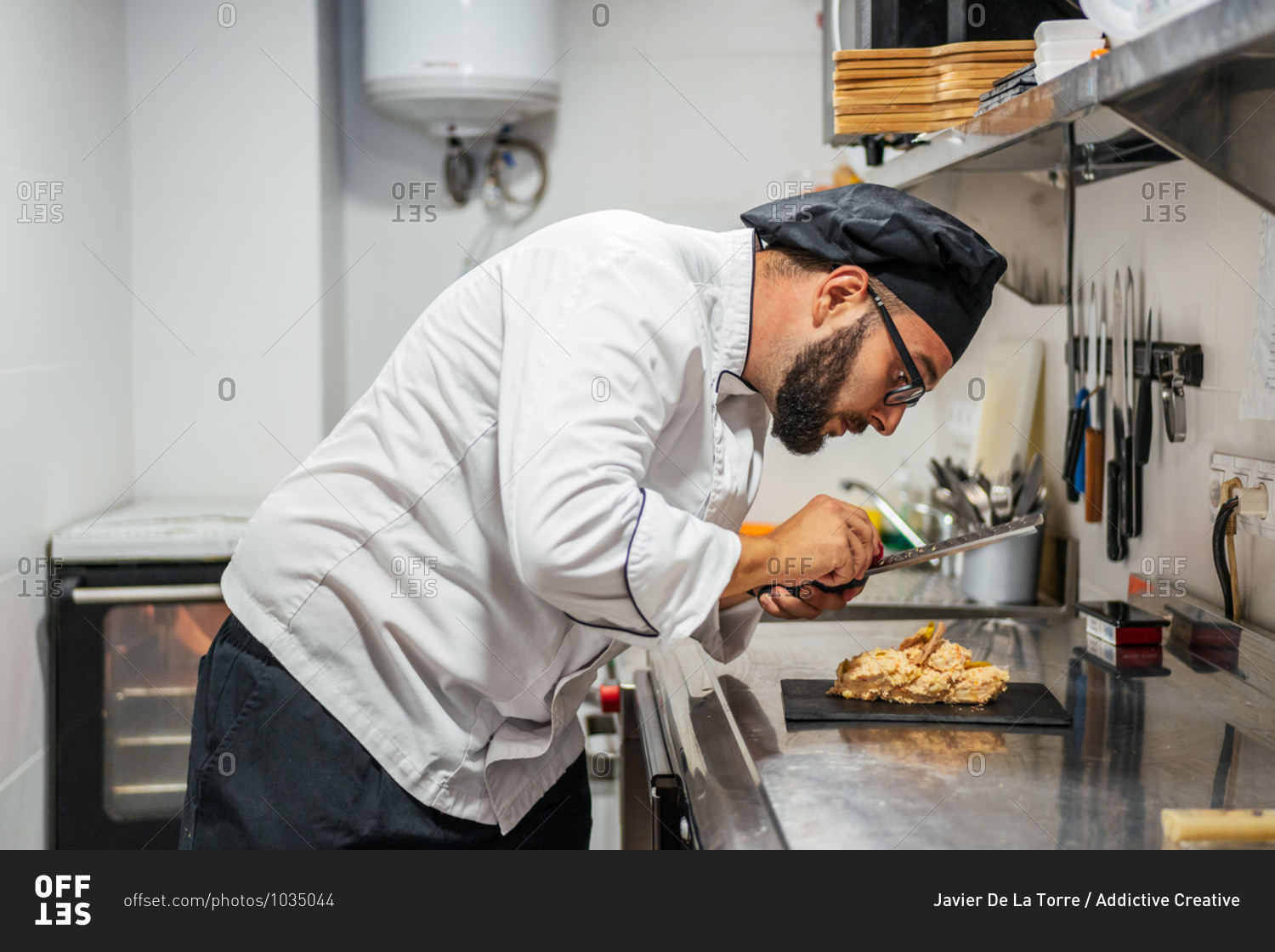 Side view of busy male cook using grater and garnishing sweet dessert placed on slate board in kitchen