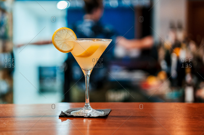 Crystal glass with delicious alcohol cocktail garnished with slice of lemon placed on wooden counter in bar