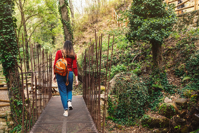 Back view of unrecognizable female traveler walking along wooden pathway in forest during summer vacation in Valle del Jerte