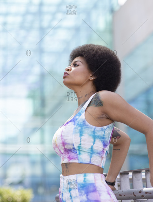 Side view of relaxed African American female standing on suspension bridge and admiring view of river in city during stroll on sunny day