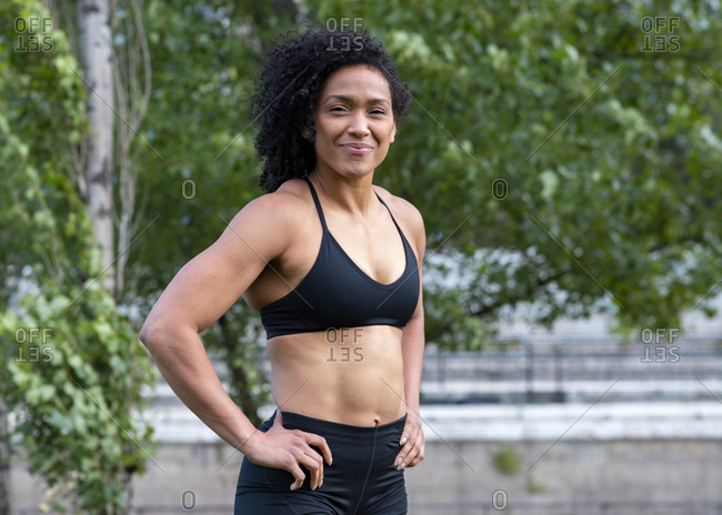Confident African American athletic female with muscular body standing with  hands on waist in city during training and looking at camera stock photo -  OFFSET