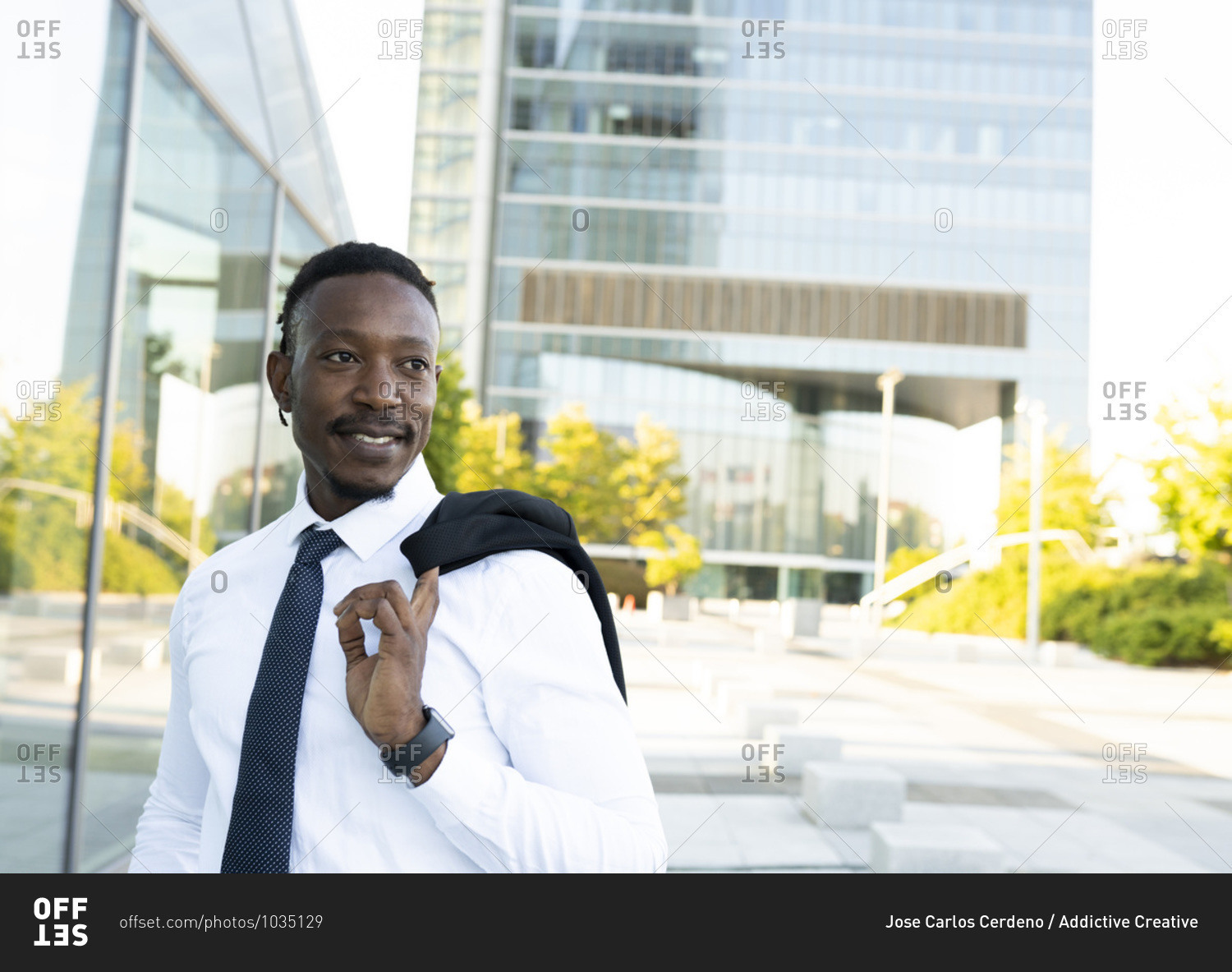 Handsome African American male entrepreneur in elegant shirt standing with jacket on shoulder in downtown and looking away