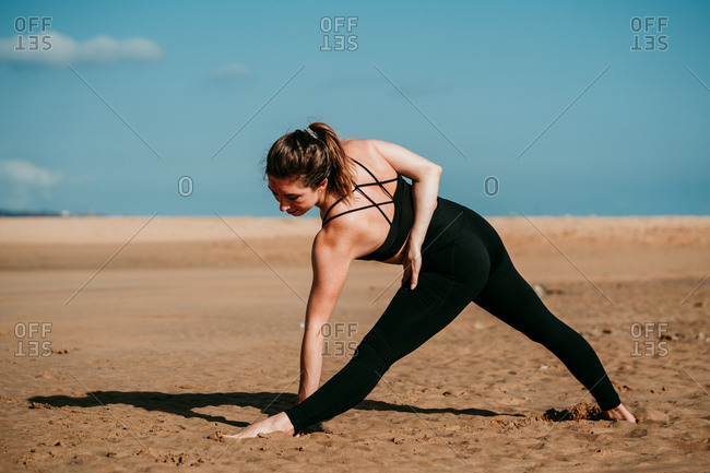 Back view of relaxed female standing barefoot on shore in Triangle pose and practicing yoga on sunny day in summer