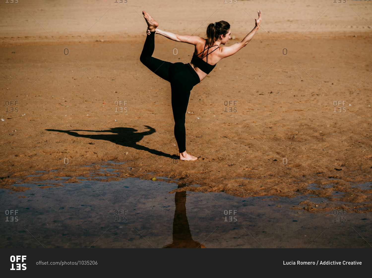 Side view of flexible unrecognizable female standing on sandy shore of river in Natarajasana and practicing yoga while balancing on leg