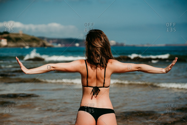 Back view of anonymous tranquil female standing in Five Pointed Star asana and doing yoga on background of amazing seascape in summer