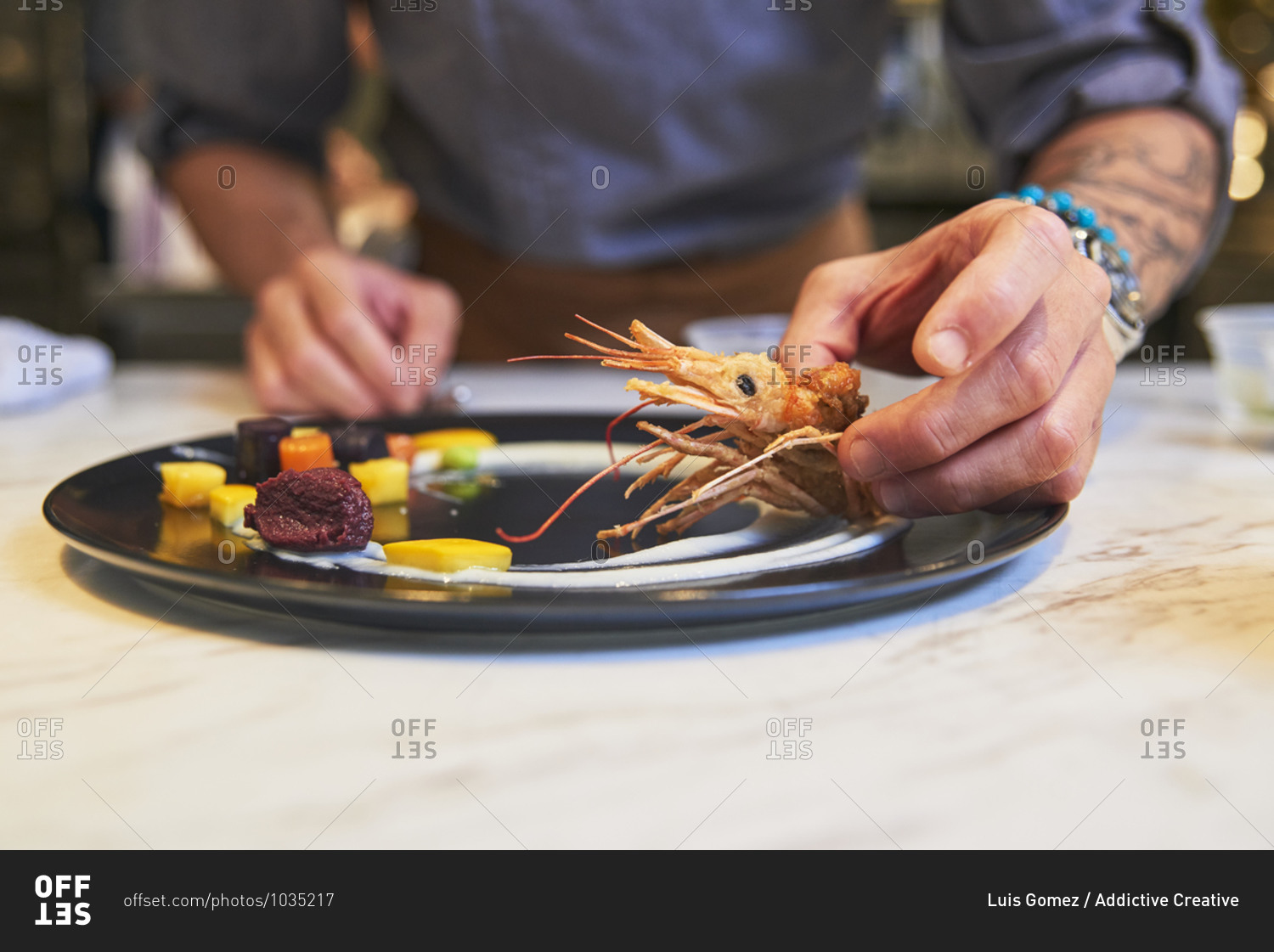 Crop anonymous chef with tongs arranging colorful edible blossoms on plate while garnishing sophisticated dish in restaurant kitchen