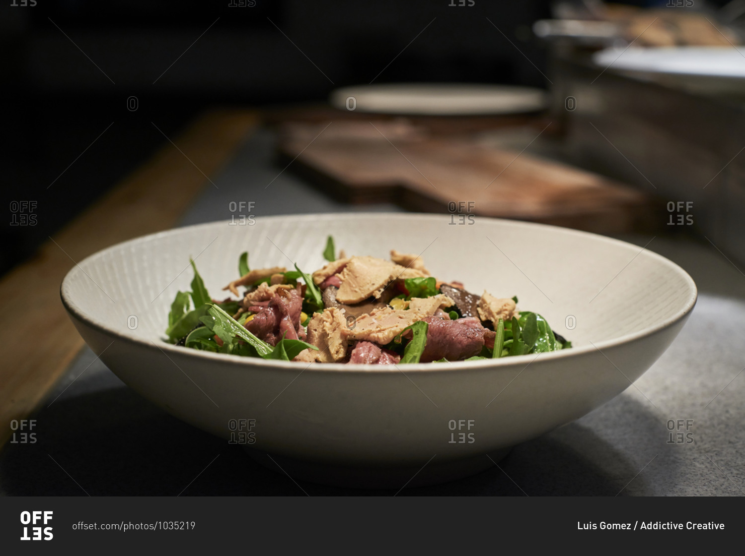 Bowl with delicious salad made with meat and fresh green rocket leaves placed on kitchen counter in restaurant
