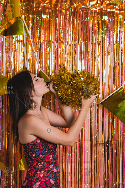 Cheerful young female in festive dress standing near foil tinsel having fun during New Year celebration