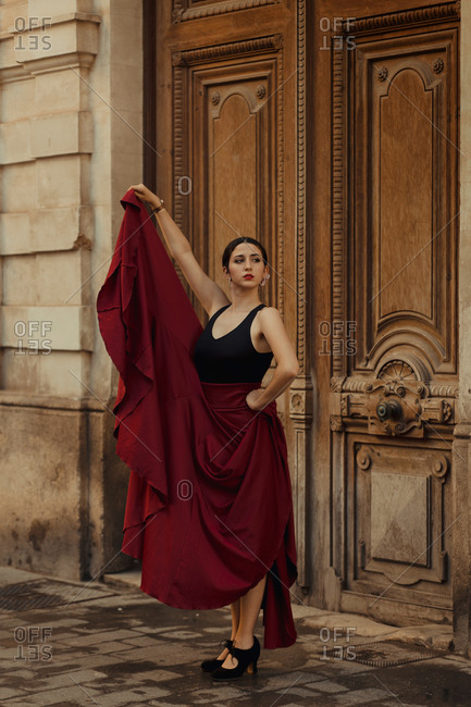 Charming young Hispanic brunette in red skirt performing traditional Flamenco dance near wooden door of old building