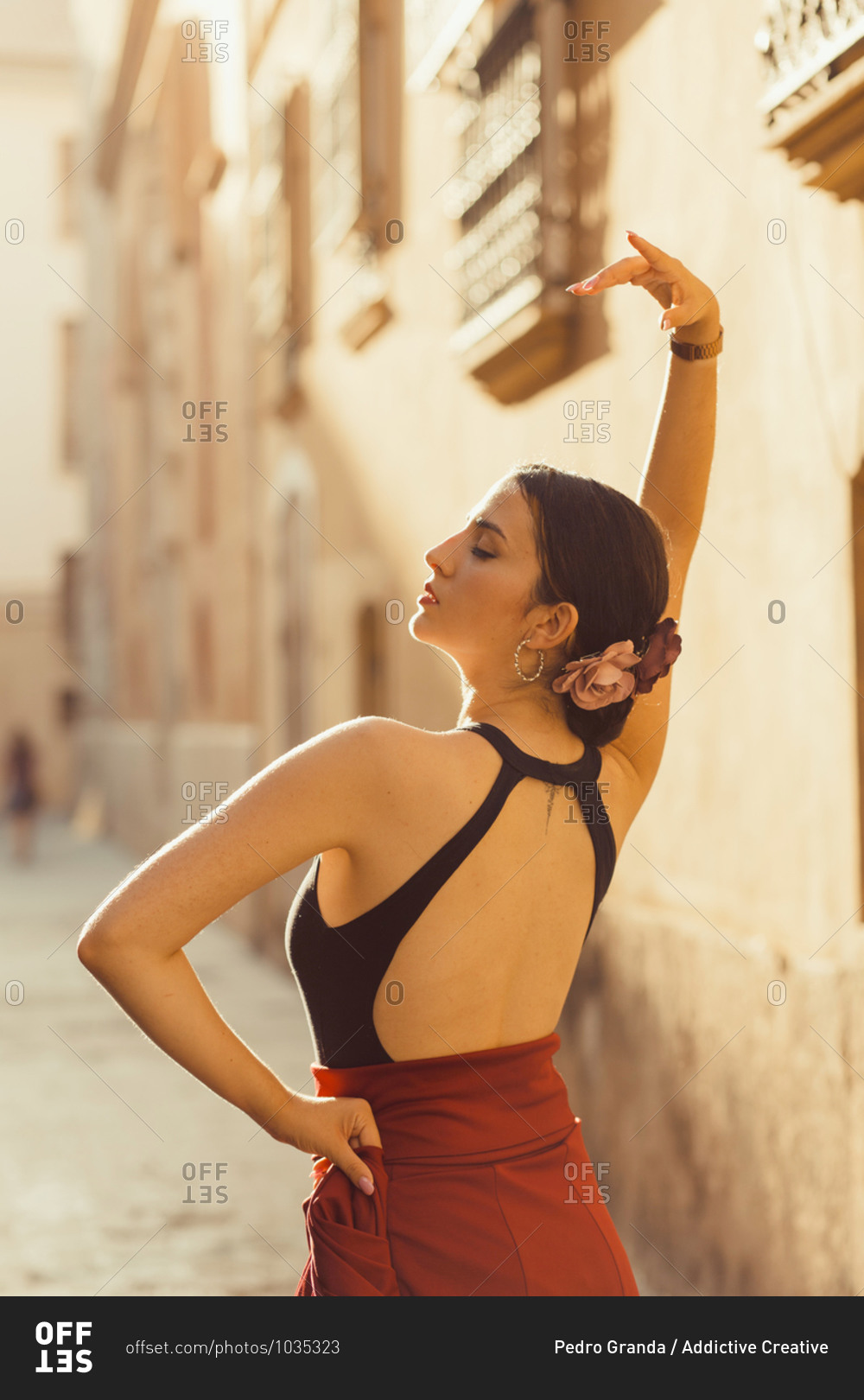 Back view of young Hispanic female dancer in traditional outfit performing Flamenco dance on old street with aged stone buildings