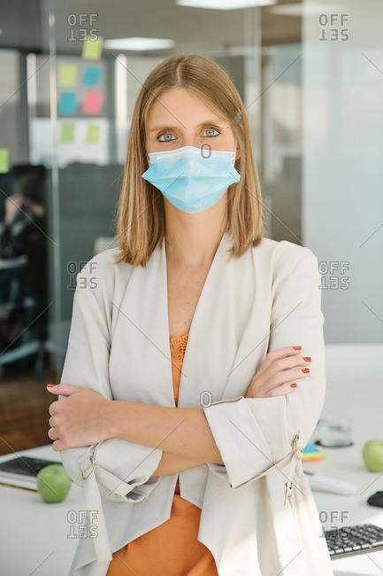 Positive young female specialist in protective mask looking at camera while standing in modern workspace