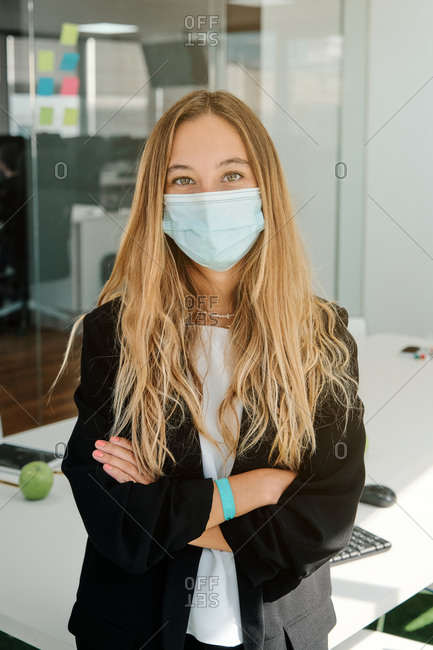 Positive young female specialist in protective mask looking at camera while standing in modern workspace